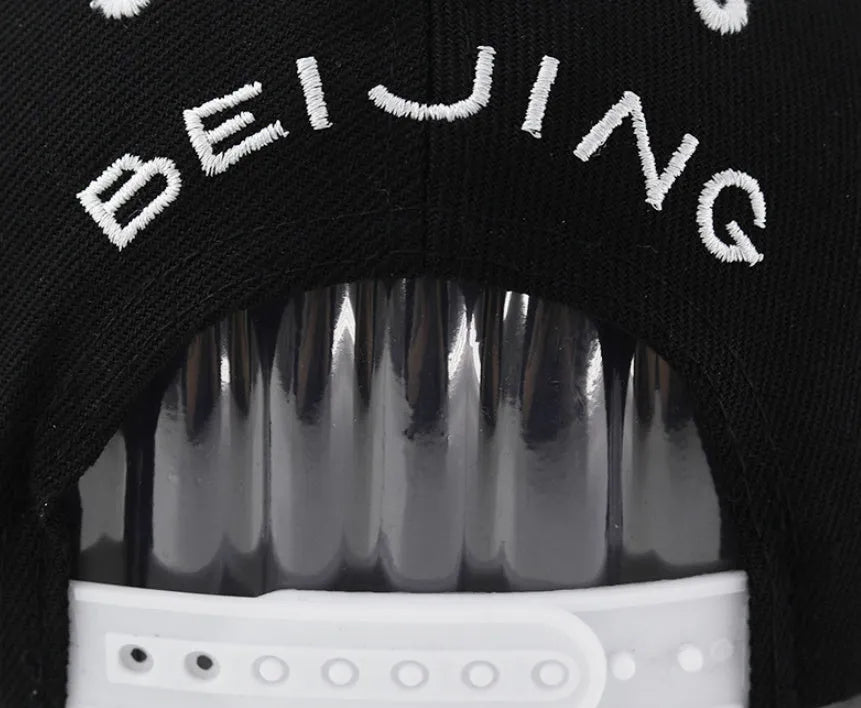 Black cotton baseball cap with white letter embroidery on the front, showing adjustable strap.