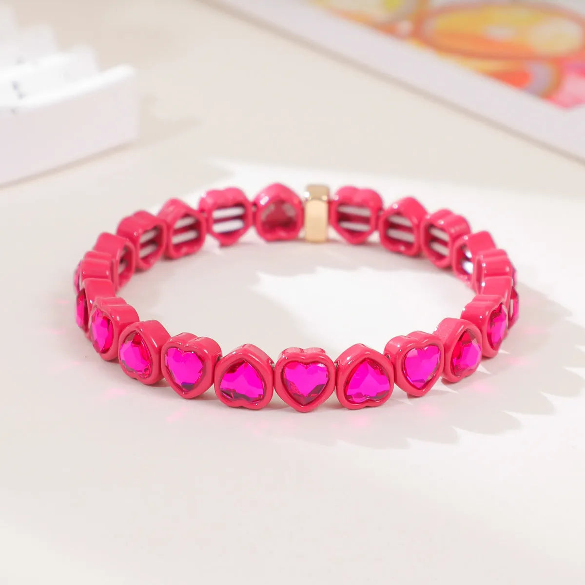 Colourful enamel heart-shaped charm on a stretch bracelet with diamond-textured alloy finish.