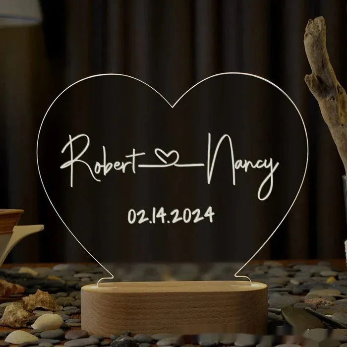 Custom transparent acrylic LED night light engraved with personal names and a date on a bedside table.