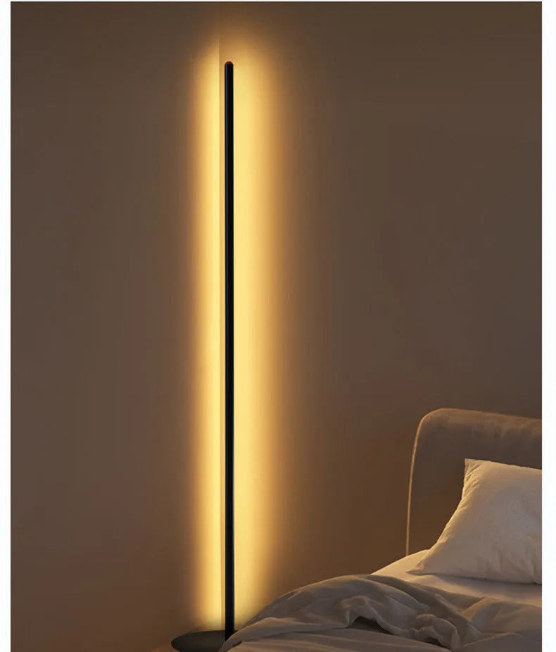 Modern vertical aluminium alloy floor lamp in silver, shown beside a sofa in a living room setting.
